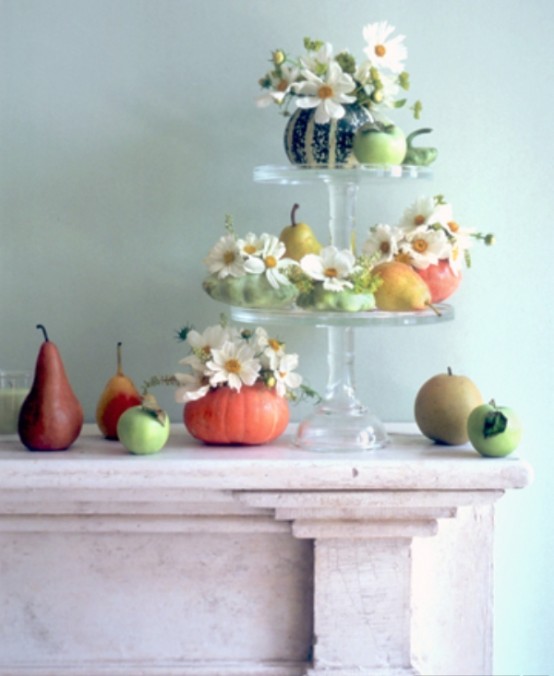 a delicate Thanksgiving centerpiece of a tiered glass stand with pumpkins and neutral blooms plus lots of fruit around is a lovely idea for a fall or Thanksgiving party