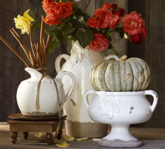 a shabby chic Thanksgiving centerpiece of jugs and bowls with red and yellow blooms and a pale green heirloom pumpkin