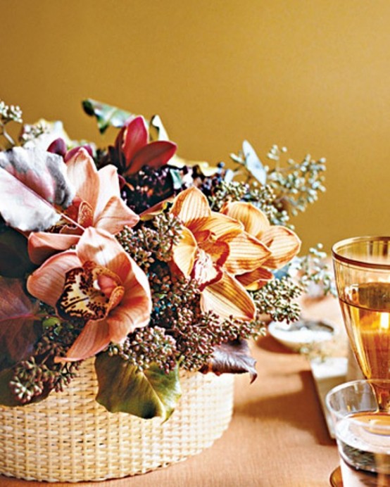 a bold Thanksgiving centerpiece of a woven basket, orange, pink and burgundy blooms, foliage and berries is a pretty and cool idea