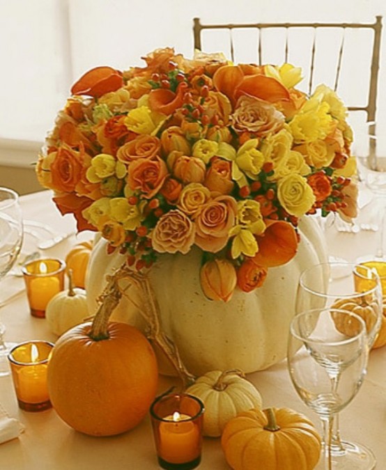 a bright fall or Thanksgiving centerpiece of a white pumpkin as a vase, orange, yellow and burgundy blooms plus berries is a cool and bold idea