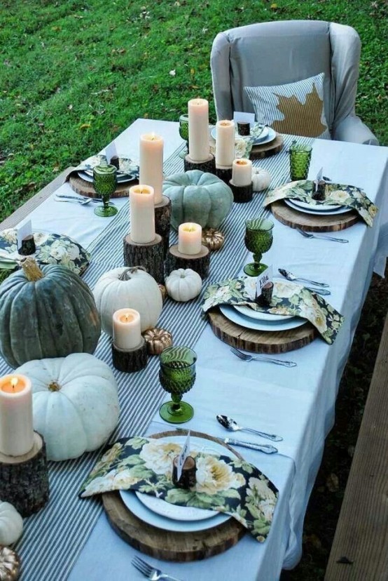a grey and green Thanksgiving tablescape with heirloom pumpkins, candles, green printed napkins and green glasses, wood slices and tree stumps