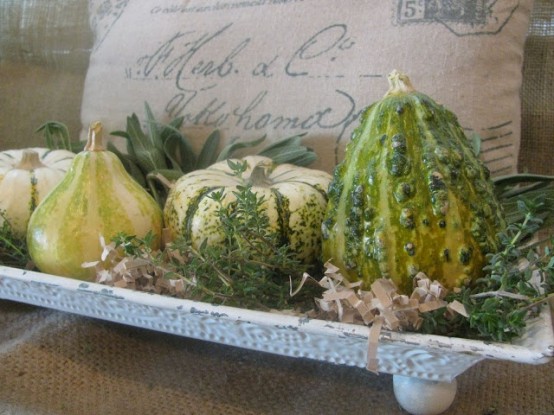 a white stand with greenery and green pumpkins and gourds is a cool Thanksgiving centerpiece or decoration with a rustic feel