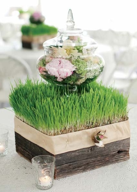 a square wooden box with wheatgrass and a jar with blooms on top plus candles around for spring decor