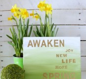 an ombre white to green spring sign with gold letters and blooms in pots is a very lovely spring decoration