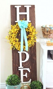 a rustic spring sign with letters, a yellow wreath and a blue bow plus potted greenery for a fresh spring feel