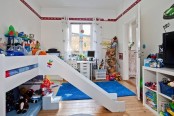 a white kid’s room with colorful decor and items, a bed with a slider, bright bedding and a rug, colorful toys and decor