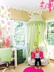 a colorful kid’s room with bright floral wallpaper, a white desk, a light green chair, a dark green cabinet and a chair with a light green canopy over it