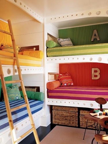a colorful shared kid's room with a grene, red, yellow and blue built-in bunk beds, a ladder and colorful and printed pillows