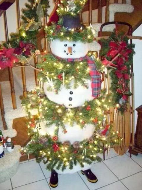 a unique snowman Christmas tree with evergreen branches with lights tucked in between the snowman parts, with pinecones, red bows and hats is a cool solution