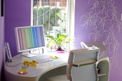 a bright home office with purple floral print walls, a curved desk, a white chair and some colorful accessories around it