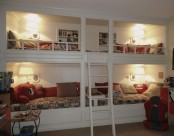 a white vintage bunk bed set of four, cozy wall lamps and a single ladder plus built-in shelves over each upper bed