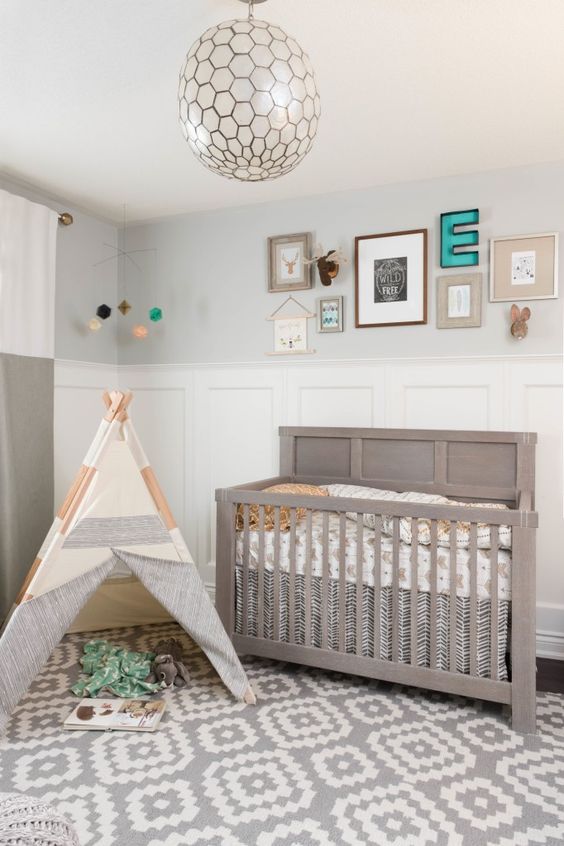 a neutral boho farmhouse nursery with paneling and grey walls, a grey crib and a teepee plus a chic gallery wall