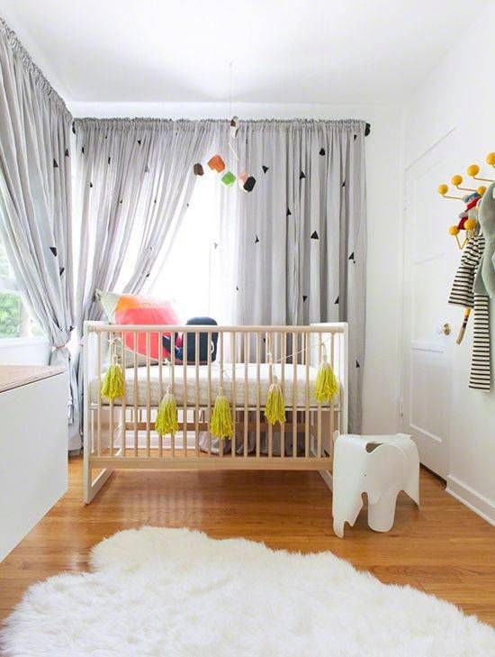 a stylish gender neutral nursery with simple and minimal furniture, grey curtains, colorful bedding and a bold mustard tassel garland