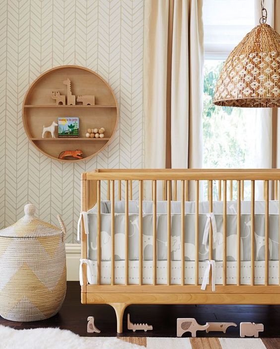 a gender neutral nursery with light-colored furniture, printed bedding, a basket and a round wooden shelf is a very chic space