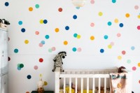 a colorful gender neutral nursery with a colorful spotted wall, bright textiles, green furniture and colorful toys