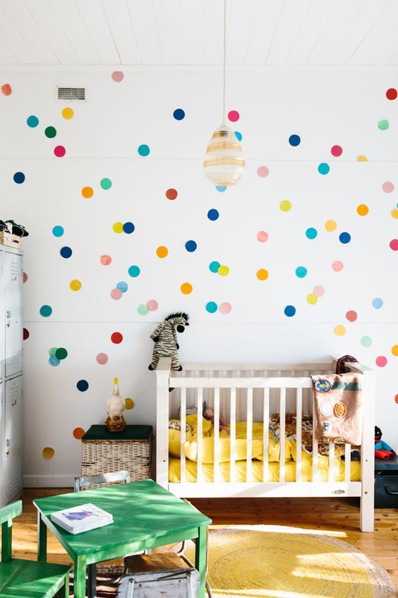 a colorful gender neutral nursery with a colorful spotted wall, bright textiles, green furniture and colorful toys