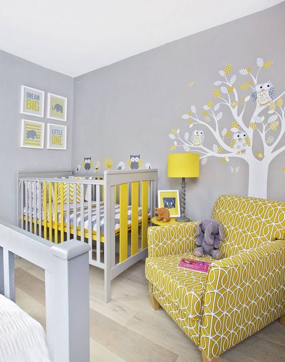 a grey nursery with bright mustard touches, a tree on the wall, a mustard printed chair and a mustard lamp is very bright and fun