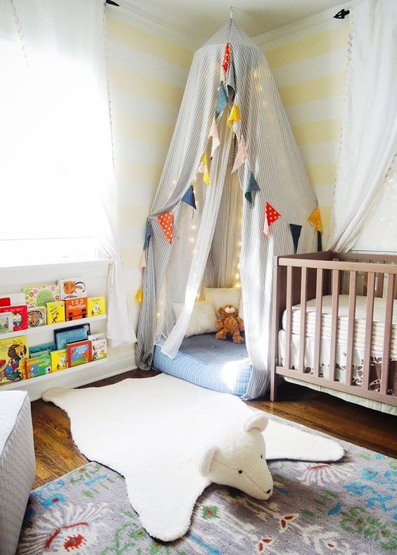 a colorful gender neutral nursery with a wooden crib, a teepee, colorful garlands and banners and bright books on the shelf