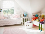 a neutral attic girl’s room with white daybeds, floral print blankets and pillows, bold toys, and a box with toys is a lovely and welcoming space