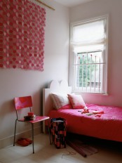 a contrasting girl’s room with all-neutral everything, hot pink bedding, a pink chair and a pink heart hanging and neutral pillows