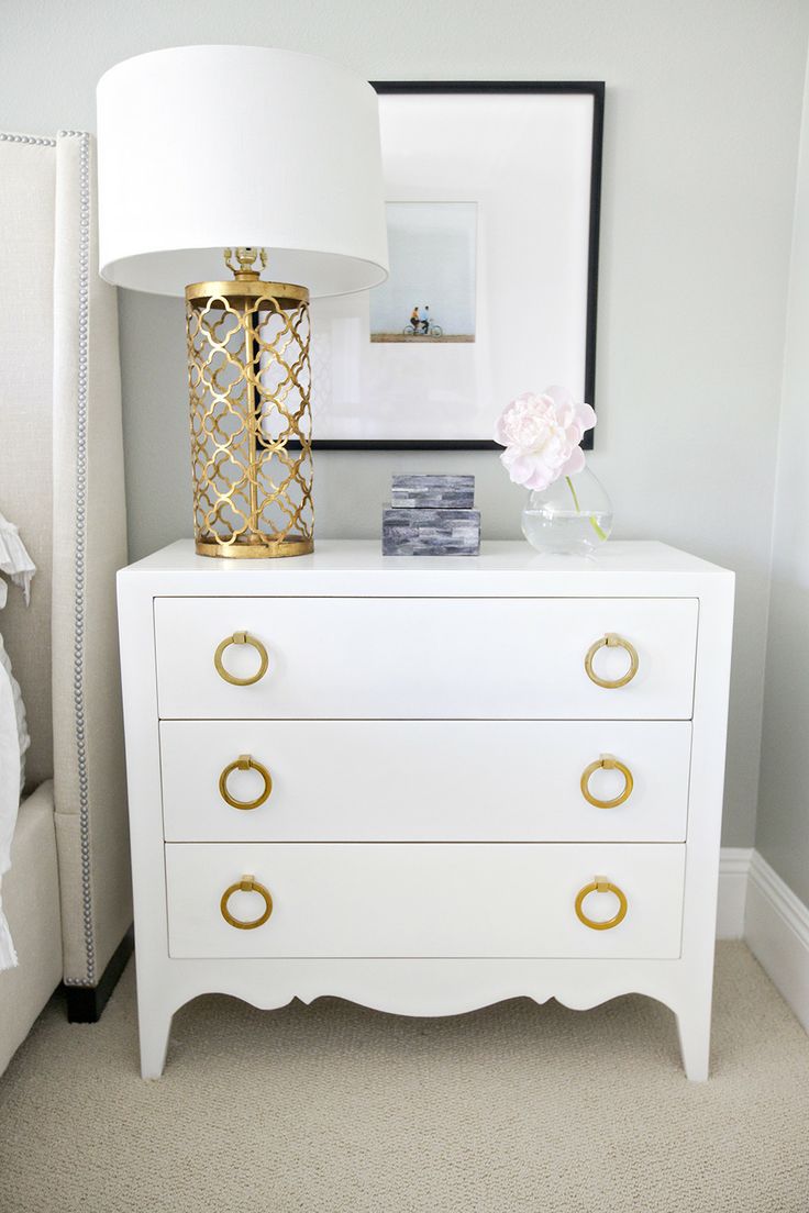a white dresser with gold ring handles and a matching chic table lamp with a refined gold base and a white lampshade give a chic touch to the bedroom