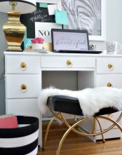 a gold sculptural lamp with a black and white lampshade, a beautiful stool with a catchy gold base and a black leather seat, a desk with gold knobs for a glam feel in the space