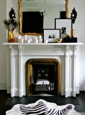 a fireplace with a gold detail, a mantel with lots of candles, gilded cnaldeholders and vases, artworks and an oversized mirror in a gilded frame for a glam feel