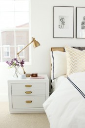 a white nightstand with gold knobs and a gold table lamp add a chic and refined feel to this neutral bedroom