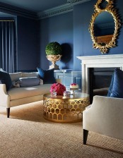 a sophisticated living room with navy walls and a ceiling, a fireplace, creamy sofas, a round coffee table with a gilded base and a mirror in a gilded frame