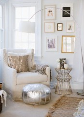 a glam reading nook with a neutral chair, a silver pouf, a gilded mini table, a glam gallery wall and a gold striped pillow and blanket