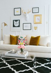 a catchy gallery wall with gold frames, prints, antlers, a gold table lamp and mustard pillows make this blakc and white room amazing