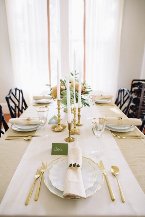 a neutral and refined Thanksgiving tablescape with neutral linens, greenery, warm-colored blooms, candles and gold cutlery for a chic touch