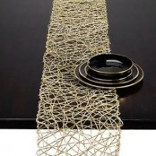 a gold woven table runner and black porcelain with a gold rim can be used for a modern Thanksgiving tablescape