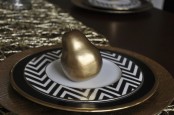 a black charger with a gold rim, chevron plates and gilded pears for a chic and stylish Thanksgiving place setting