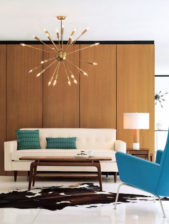 a mid-century modern living room with a plywood wall, a creamy sofa, a turquoise chair, a low coffee table, a sunburst chandelier and a cowhide rug