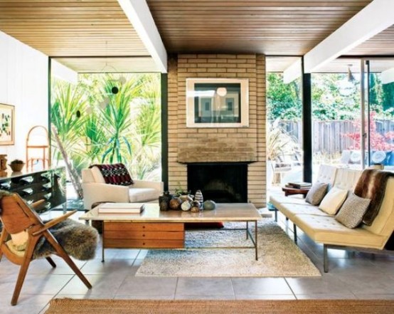 a mid-century modern living room with a brick fireplace, neutral seating furniture, stained furniture and glass walls for indoor-outdoor living