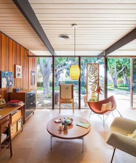 a mid-century modern living room with a wood clad wall and glazed ones, stained storage furniture and seating furniture, a low coffee table, cool artwork