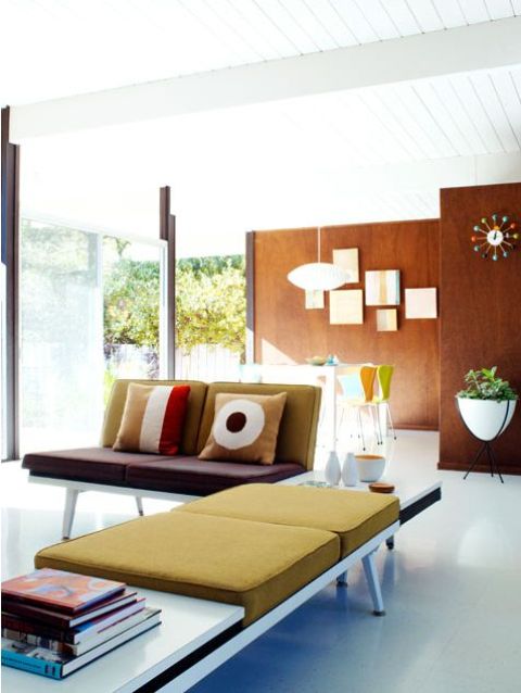 a bold mid-century modern living room with plywood walls, glazed walls for indoor-outdoor living room with a mustard couch with books and pillows