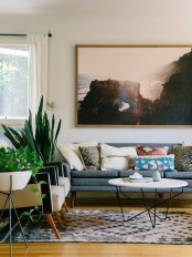 a pretty mid-century modern living room with a grey sofa, bright pillows, a printed rug, potted greenery and a print is amazing