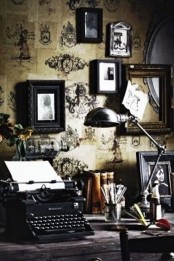 an exquisite home office with vintage print wallpaper, a black desk and a vintage gallery wall, a table lamp, some books and a black chair
