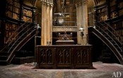 a Gothic library with bookshelves raising up to the ceiling, curved staircases, a heavy carved desk in the center and a chair – the whole space looks like out of a movie
