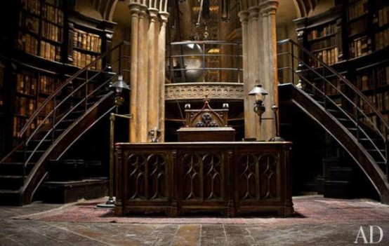 a Gothic library with bookshelves raising up to the ceiling, curved staircases, a heavy carved desk in the center and a chair - the whole space looks like out of a movie