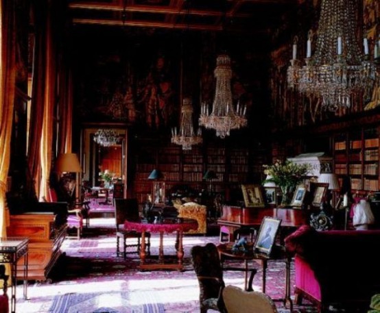 a bold Gothic library with lots of bookshelves covering two walls, refiend crystal chandeliers, fuchsia and purple furniture and refined carved tables and chairs