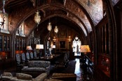 a vintage gothic library with bookcases covering the walls, a long table with refined chairs, pendant lamps, floor lamps and a refined sofa