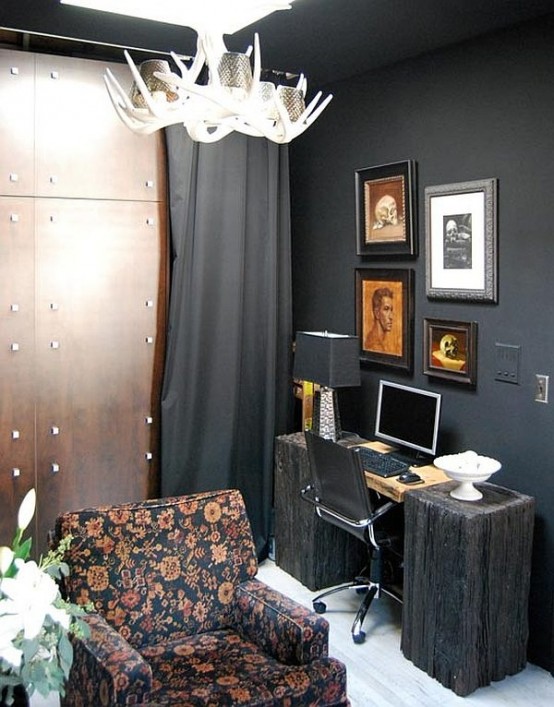 a modern home office with a Gothic feel, black walls and a ceiling, a quirky desk, a modern chair and a floral one, an antler chandelier and a vintage gallery wall