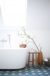 a Scandinavian bathroom with blue geometric tiles on the floor, white large scale tiles on the walls and wooden touches for more coziness