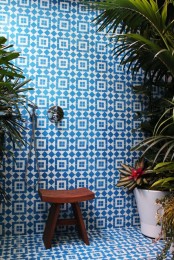 a bright tropical blue and white geometric tile bathroom with a wooden stool and lots of potted plants and blooms around