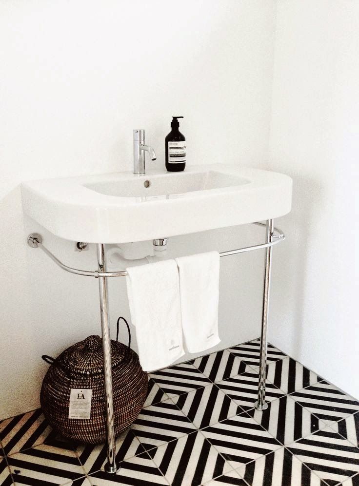 a stylish bathroom with a black and white geometric tile floor and a free standing sink is chic and bold
