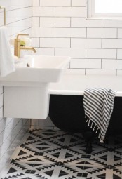 a retro bathroom with a black and white geo tile floor, a black clawfoot tub and a wall-mounted sink for a chic look