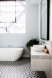 an eclectic bathroom with black and white geometric tiles on the floor, white beadboard walls, a floating vanity with a whiet stone countertop